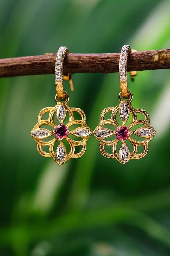 Pair of gold openwork blossom earrings with pink stones hanging from a branch